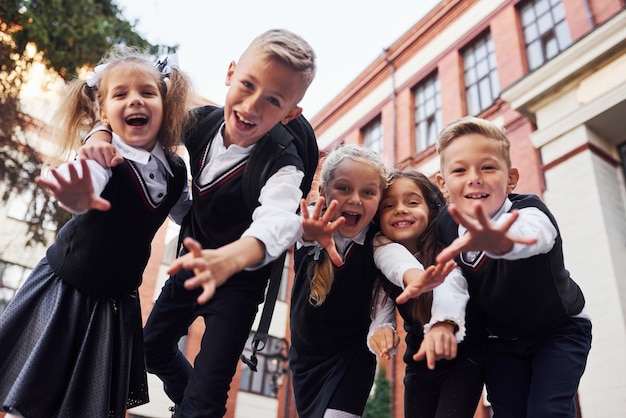 Plezier maken en elkaar omhelzen. Groep kinderen in schooluniform dat buiten samen is in de buurt van het onderwijsgebouw.