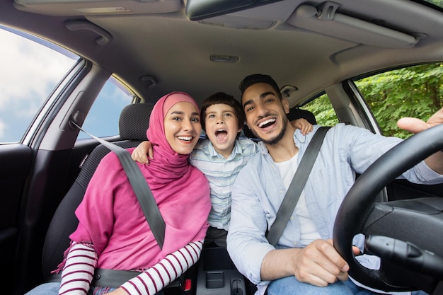 Plezier op de weg. Vrolijke moslimfamilie van drie die samen in de auto zingen