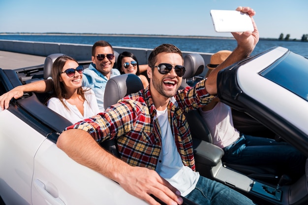 Plezier vastleggen. groep jonge gelukkige mensen die genieten van een roadtrip in cabrio en selfie maken