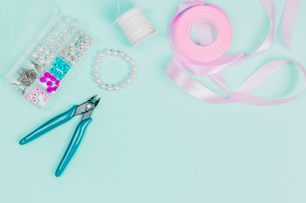 Photo pliers; pearls; thread spool and pink ribbon on teal background