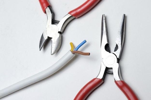 Pliers and stripped three-core wire on a white background close-up.