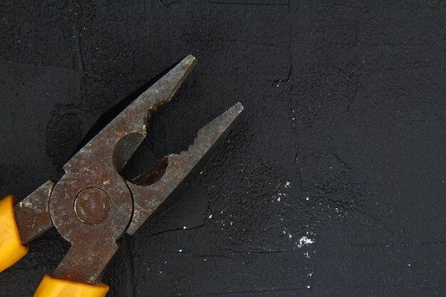 Pliers with a yellow handle on a black stone background Pliers nippers isolated on black