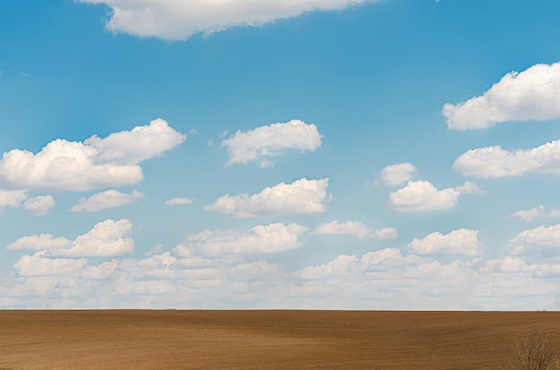 Plowed empty field, blue sky with clouds.