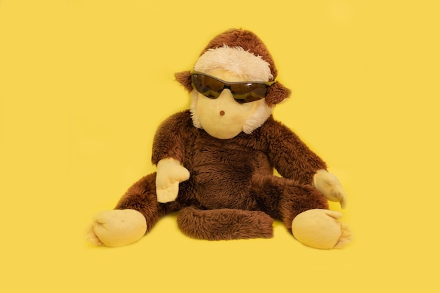 Pluche aap met zonnebril gekleed op een gele achtergrond