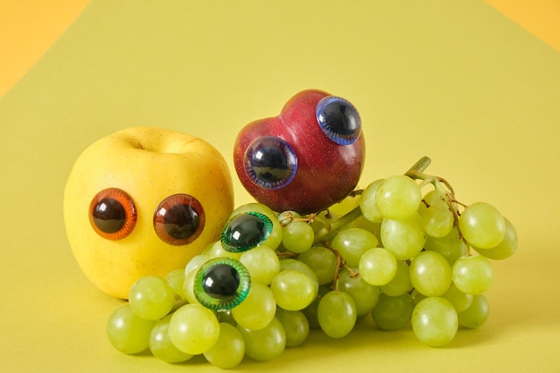 Plum apple and bunch of grapes with puppet eyes prank concept
green background cute fruit faces