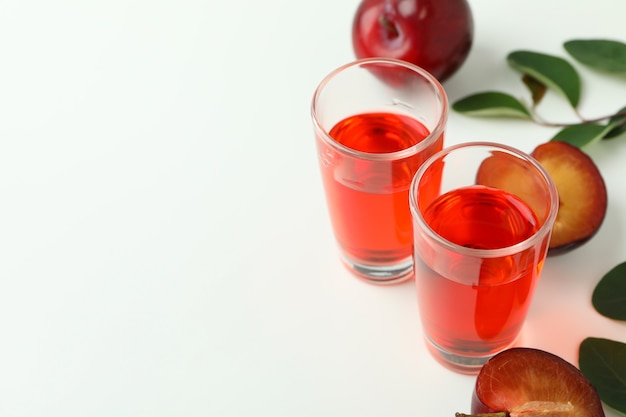 Plum brandy shots and ingredients on white background