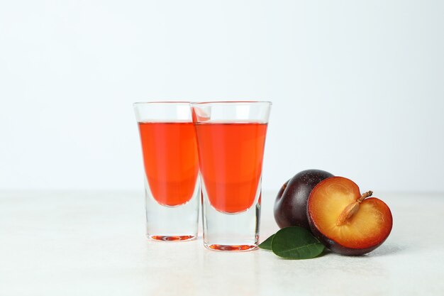 Plum brandy shots and ingredients on white textured table