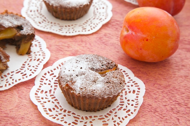 Plum chocolate cake with sugar powder on a decorative white napkin. Fresh plum in the background