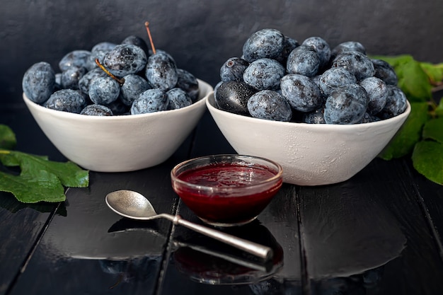 Plum jam in a jar. In the background there are plums. Tkemali sauce. Getting ready for winter. Dark background.