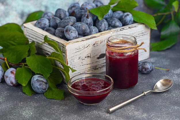 Plum jam in a jar. In the background there are plums. Tkemali sauce. Preparing for winter. Light background.