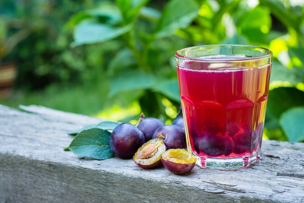 Plum juice in glass on wooden table background. Natural Green Leaf Background. Copy sapce.