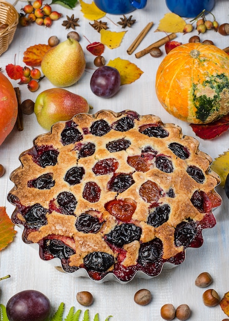 Plum pie on a light autumn background, with fallen leaves, fruits, nuts, pumpkin. Flat lay.