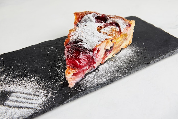 Plum pie with kinaman sprinkled with powdered sugar on black stone