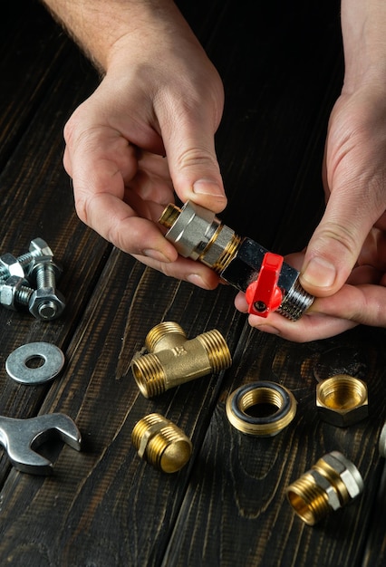 A plumber connects brass fittings to a water tap closeup of a master hand while working in a workshop