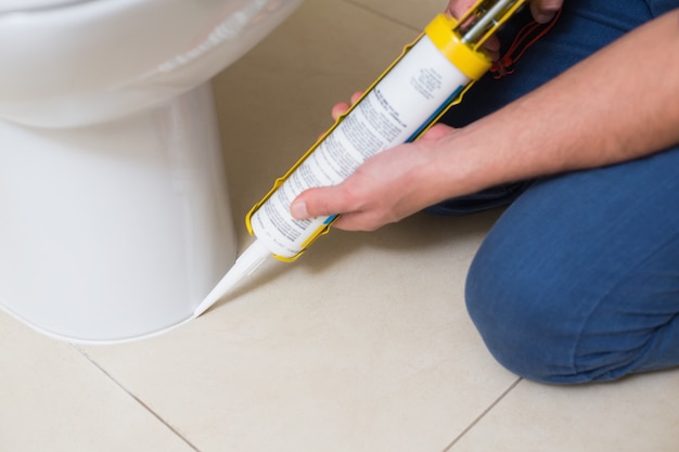 Photo plumber fixing toilet in a washroom with silicone cartridge