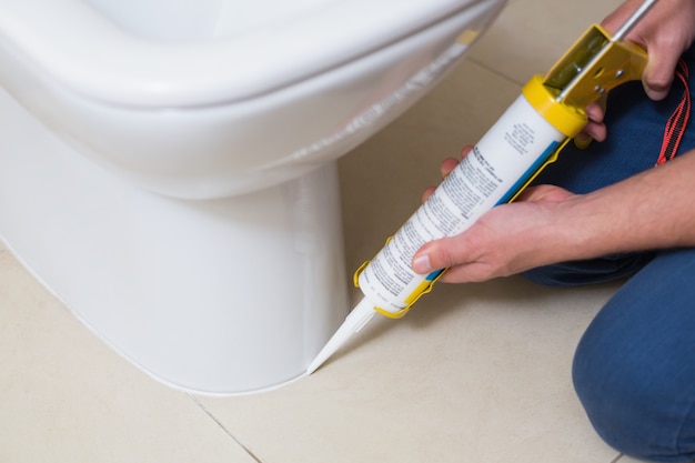 Plumber fixing toilet in a washroom with silicone cartridge