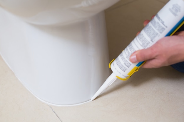 Photo plumber fixing toilet in a washroom with silicone cartridge