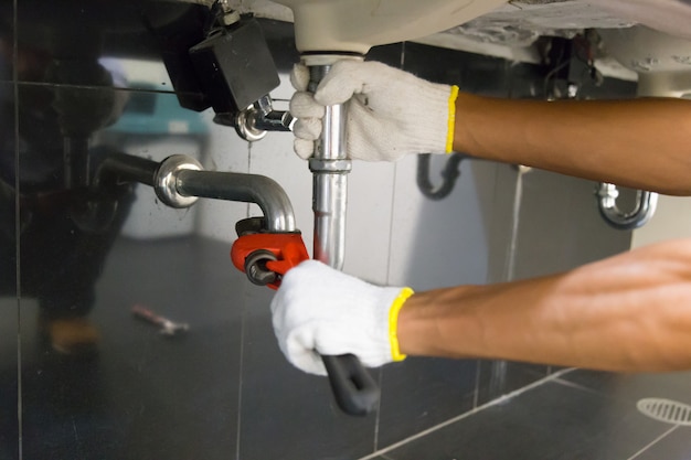 Photo plumber fixing white sink pipe with adjustable wrench.