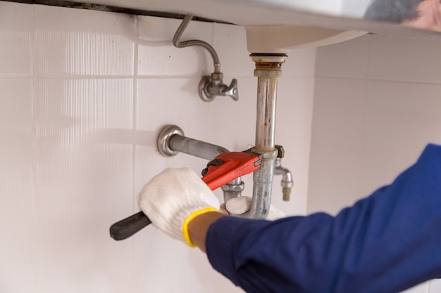 Plumber fixing white sink pipe with adjustable wrench