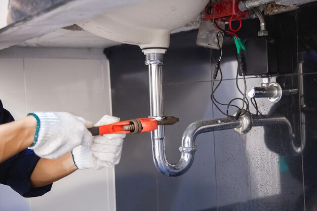 Photo plumber fixing white sink pipe with adjustable wrench