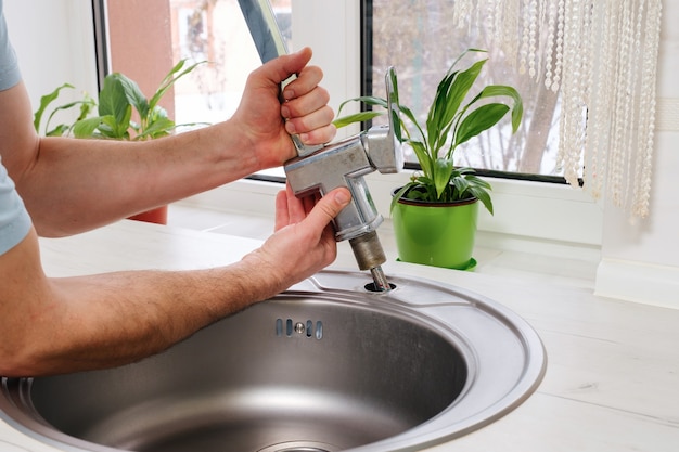 Plumber hands removes the old faucet from the kitchen sink