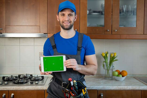 Plumber holds a digital tablet with a green screen in the kitchen