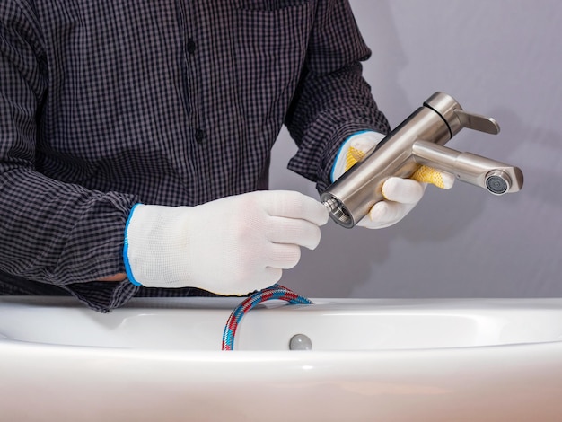 A plumber installs a faucet in a bathroom connects a hose to the faucet closeup