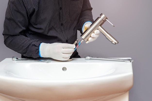 A plumber installs a faucet in a bathroom connects a hose to the faucet closeup