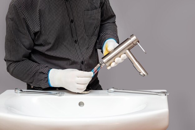 A plumber installs a faucet in a bathroom connects a hose to the faucet closeup