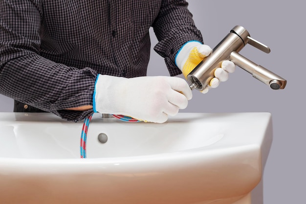 A plumber installs a faucet in a bathroom connects a hose to the faucet closeup