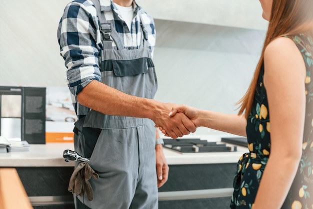 plumber in uniform helped woman on the kitchen doing handshake