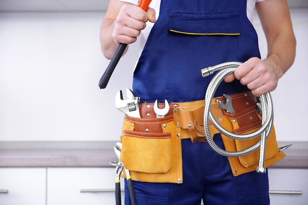 Photo plumber in uniform holding pipe wrench at kitchen