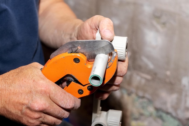 A plumber uses a special scissors to cut a polypropylene pipe during the installation of a water pipe