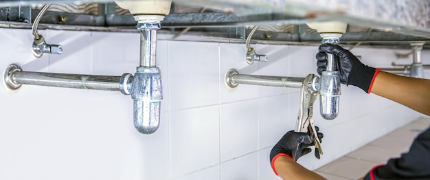 Photo plumber using a wrench to repair a water pipe under the sink