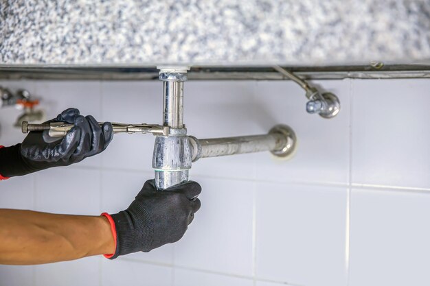 Plumber using a wrench to repair a water pipe under the sink