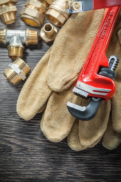 Plumbing monkey wrench pipe connectors protective gloves water valve on wooden board.