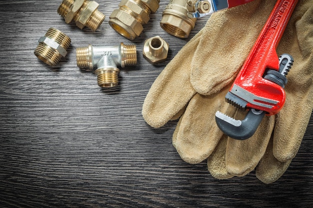 Photo plumbing monkey wrench pipe fittings protective gloves water valve on wooden board.