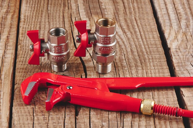 Plumbing supplies on a wooden background. Red gas wrench and faucets.