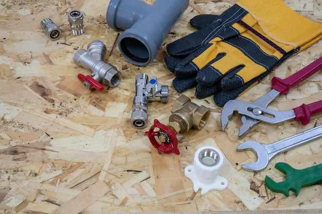 Plumbing tools parts pipeline components and gloves on the background of a construction OSB plate