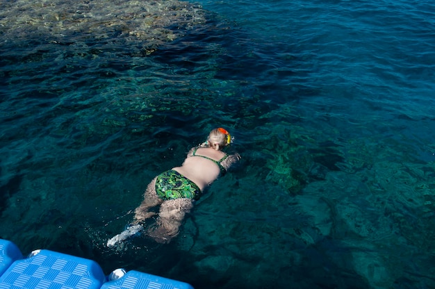 Plump girl in a green swimsuit and a swimming mask dives and swims in the sea