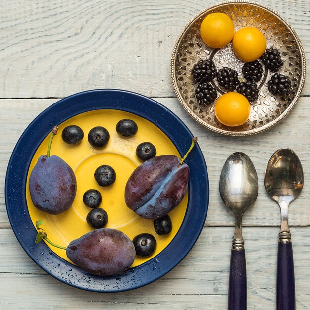 Plums and blueberries in a plate on a white wooden table