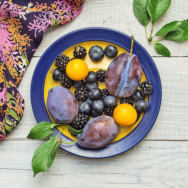 Plums and blueberries in a plate on a white wooden table