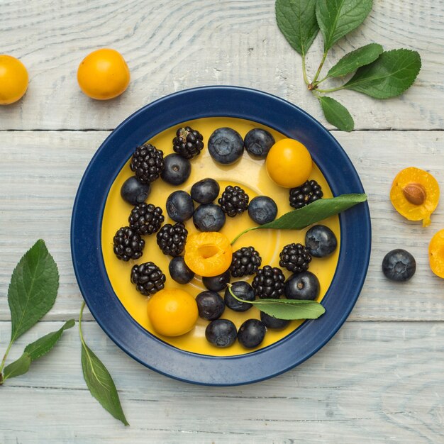 Plums and blueberries in a plate on a white wooden table