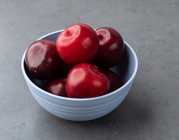 Plums in a bowl over stone background.