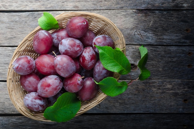 Plums in a wicker basket on old wooden background