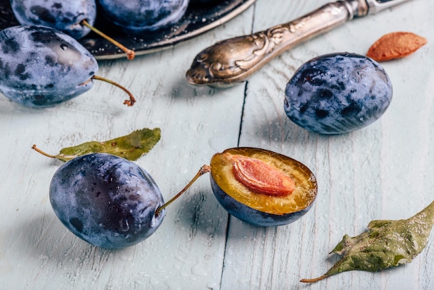 Plums with leaves and knife over wooden surface