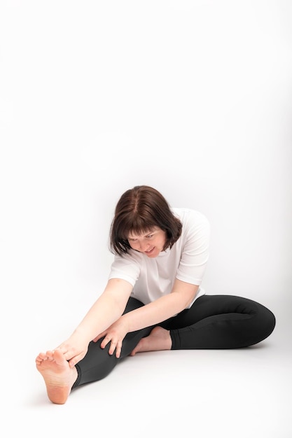 Plus grootte jonge donkerbruine vrouw die uitrekkende oefening doet. Portret van meisje op witte achtergrond die zich bezighouden met gymnastiek.