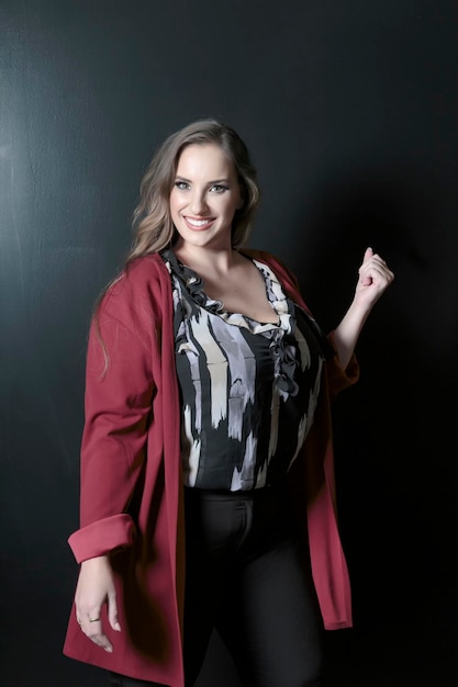 Plus size attractive lady posing and standing against dark backdrop with charming smile Perfect makeup fashion beauty portrait Beautiful smiling brunette big size woman with brown long hair