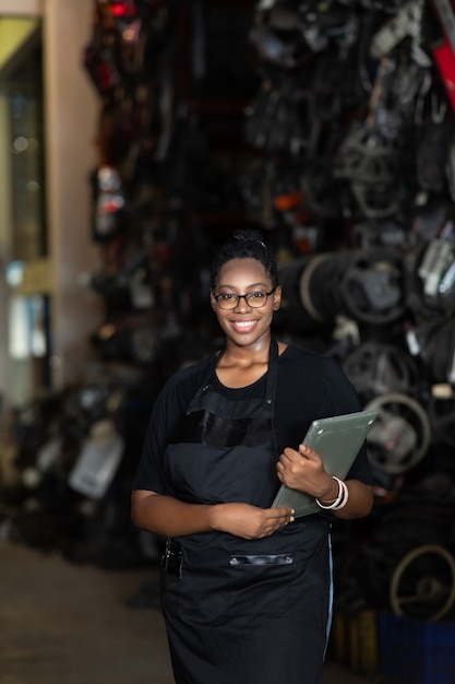 Plus size black female worker inspecting old car parts stock while working in automobile large warehouse