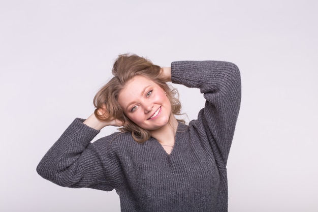 Plus-size female model with hand in hair wearing gray sweater on white.